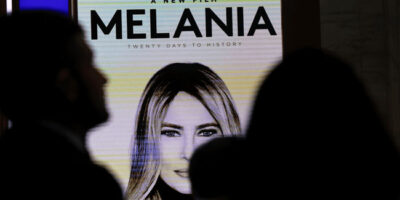 Melania digital poster photographed from afar with the silhouette of people between the photographer and the poster.