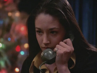 A brunette teenage girl looks fearful while holding a corded 1970s telephone to her ear in the film, Black Christmas (1974).