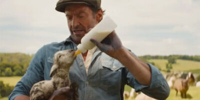 Hugh Jackman feeds a lamb milk from a bottle in the 2026 film, The Sheep Detectives.