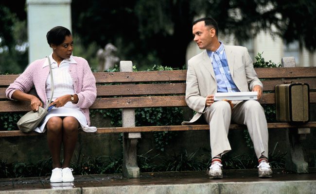 Tom Hanks sitting on a park bench talking to a female nurse who is sat next to him in the film Forrest Gump
