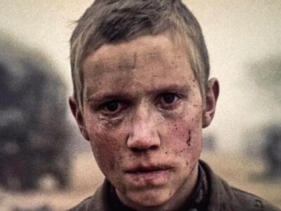 A sad-looking young boy is pictured in profile, his muddy face showing signs of bloody injury and bruising, from the film Come and See.