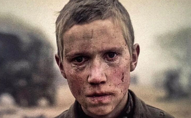 A sad-looking young boy is pictured in profile, his muddy face showing signs of bloody injury and bruising, from the film Come and See.
