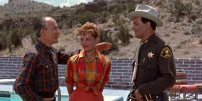 A vibrant 2.55:1 CinemaScope still from Edge of Eternity featuring Cornel Wilde and Victoria Shaw against a desert backdrop.