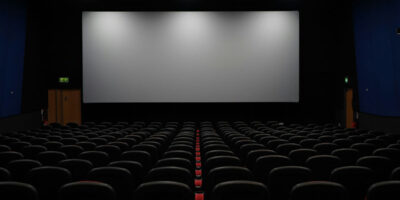 Inside an empty movie theatre, looking from the back row towards a blank screen.