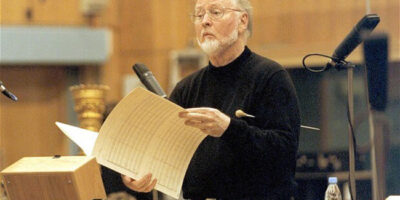 John Williams holding sheet music and working with an orchestra