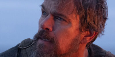 Matt Damon, bathed in a low, red-orange sunset glow, and sporting a thick beard, in the film The Odyssey.