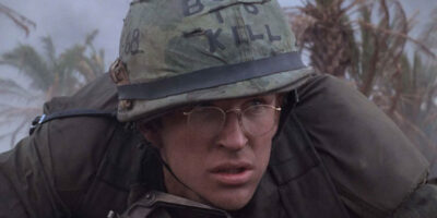 Matthew Modine in the film Full Metal Jacket is seen ducking for cover in military uniform with a helmet that says "Born to Kill"