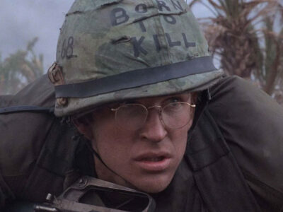 Matthew Modine in the film Full Metal Jacket is seen ducking for cover in military uniform with a helmet that says "Born to Kill"
