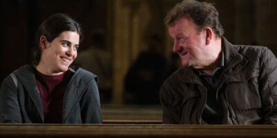 Actors Ebla Mari and Dave Turner share a smile, sitting next to each other in the Ken Loach film, The Old Oak.