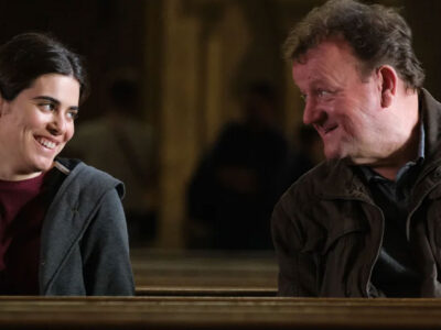 Actors Ebla Mari and Dave Turner share a smile, sitting next to each other in the Ken Loach film, The Old Oak.