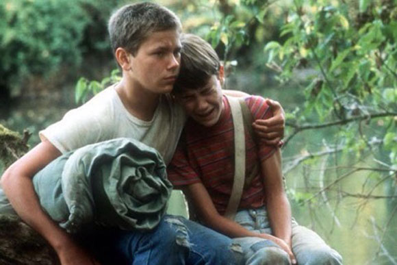 Actors Wil Wheaton and River Phoenix in the film Stand by Me - the two teenage boys sit in a woodland with Phoenix having his arm around Wheaton who is crying.