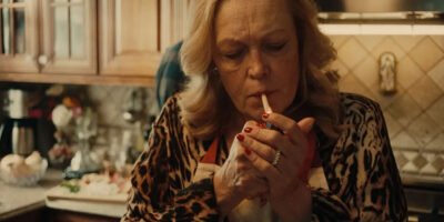 Cathy Moriarty lights a cigarette while standing in a small, cluttered kitchen in the 2025 short film, Sunday Sauce.