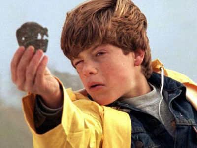 Sean Astin as the character Mikey Walsh in the film The Goonies wearing a bright yellow raincoat.